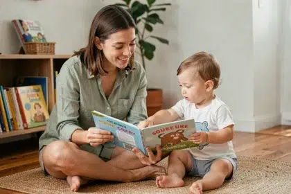 Une femme accompagne un jeune enfant dans l'apprentissage du langage en lisant un livre illustré ensemble sur un tapis de jeu