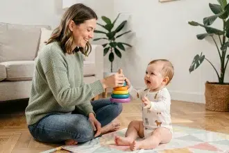 Mère souriante jouant avec son bébé de 7 mois avec un jouet en bois coloré sur un tapis de jeu pastel dans un salon scandinave